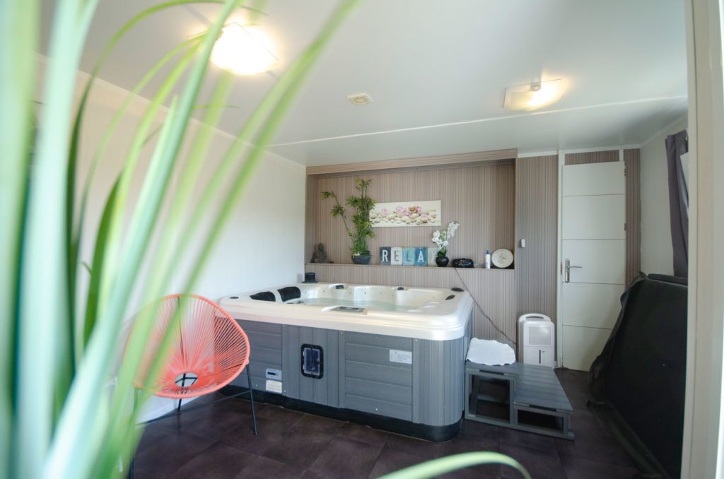 A modern bathroom with a large bathtub, a small sink, and a shower area. There are plants and decorative items on the wall, and a towel rack is visible.