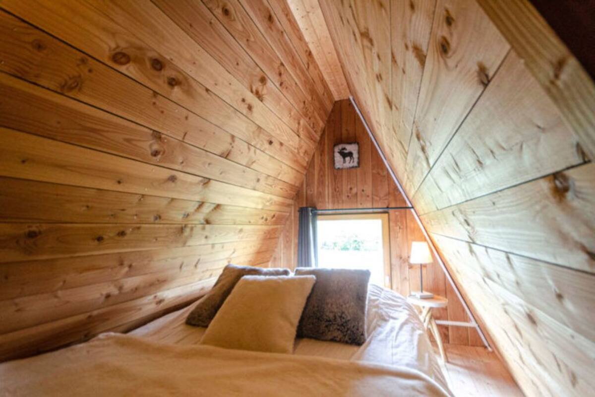 Een gezellig slaapkamer onder het dak met houten wanden, een bed met kussens, een nachtkastje en een raam met uitzicht.