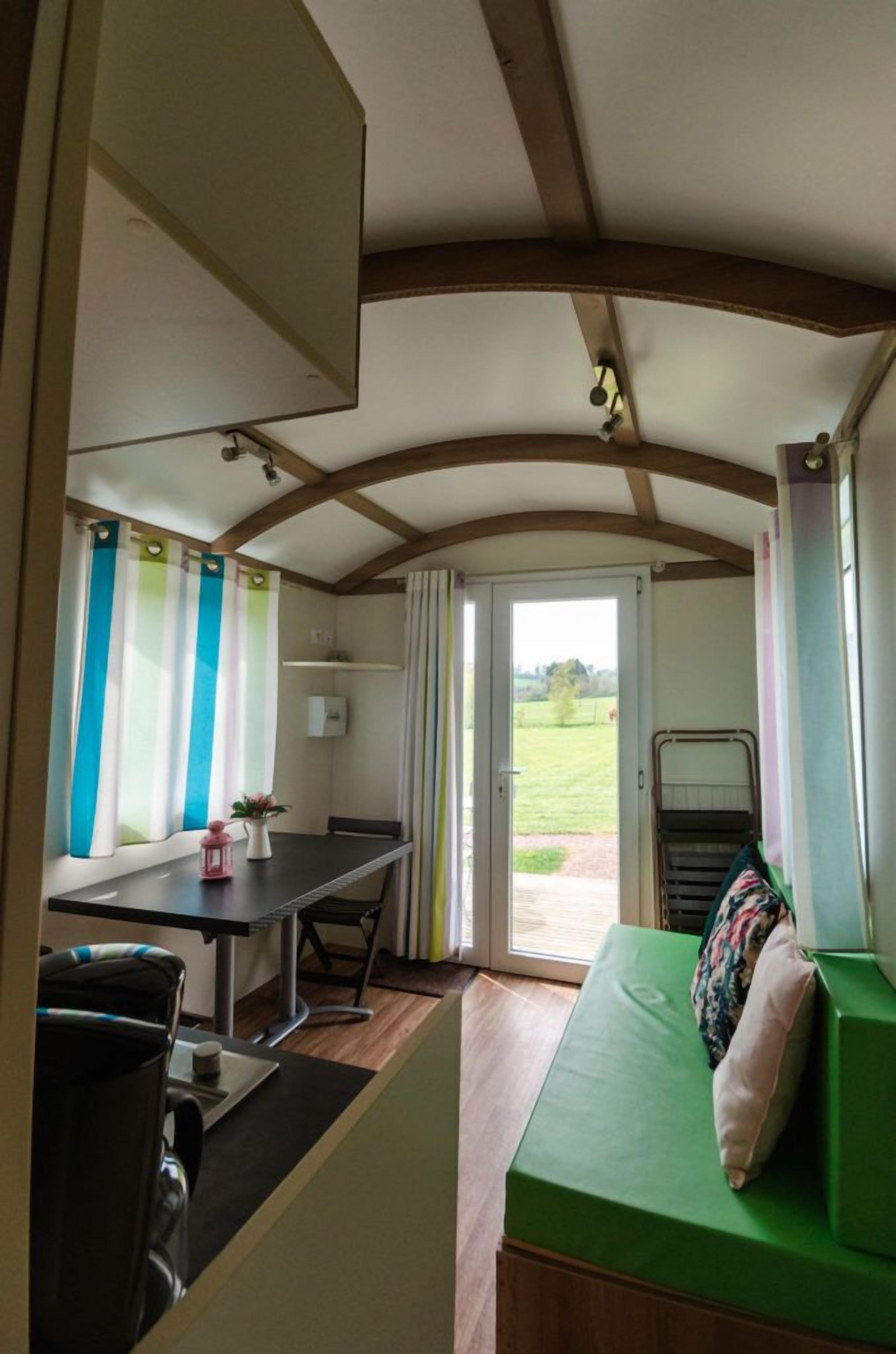 Une pièce chaleureuse avec une table à manger, des chaises, un canapé vert et une vue sur l’extérieur.