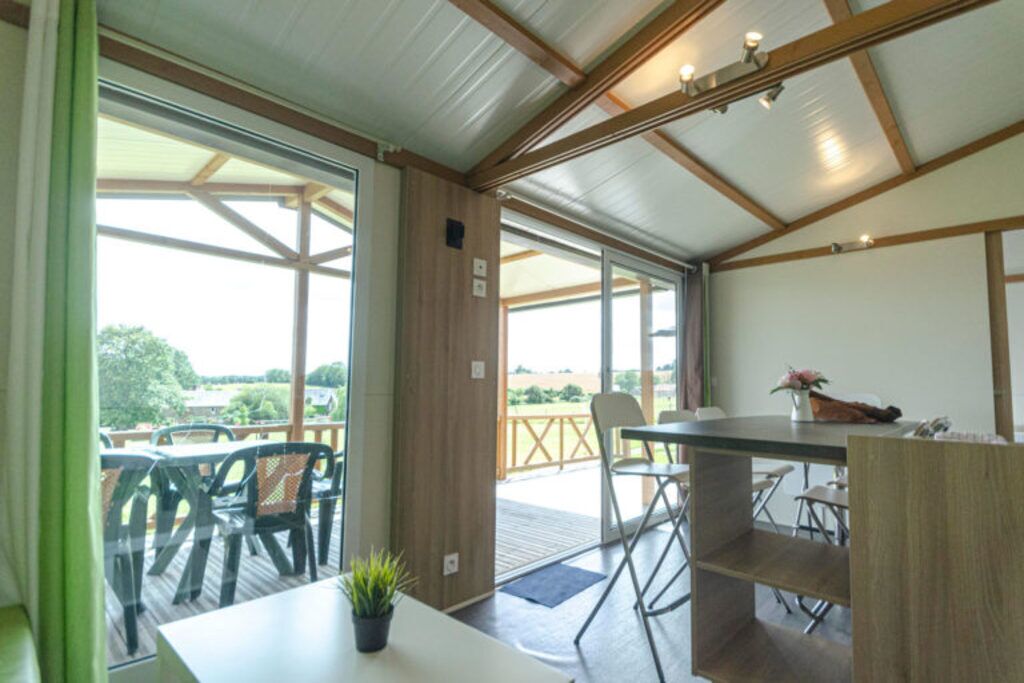 Un espace extérieur abrité, aménagé pour prendre les repas, avec une table et des chaises, un pot de fleurs et une vue sur l’extérieur.