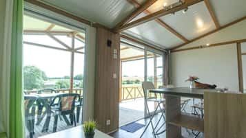 Un espace extérieur abrité, aménagé pour prendre les repas, avec une table et des chaises, un pot de fleurs et une vue sur l’extérieur.