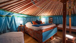 Een traditioneel yurt interieur met een centraal bed, een kleiner bed en een houten kast.