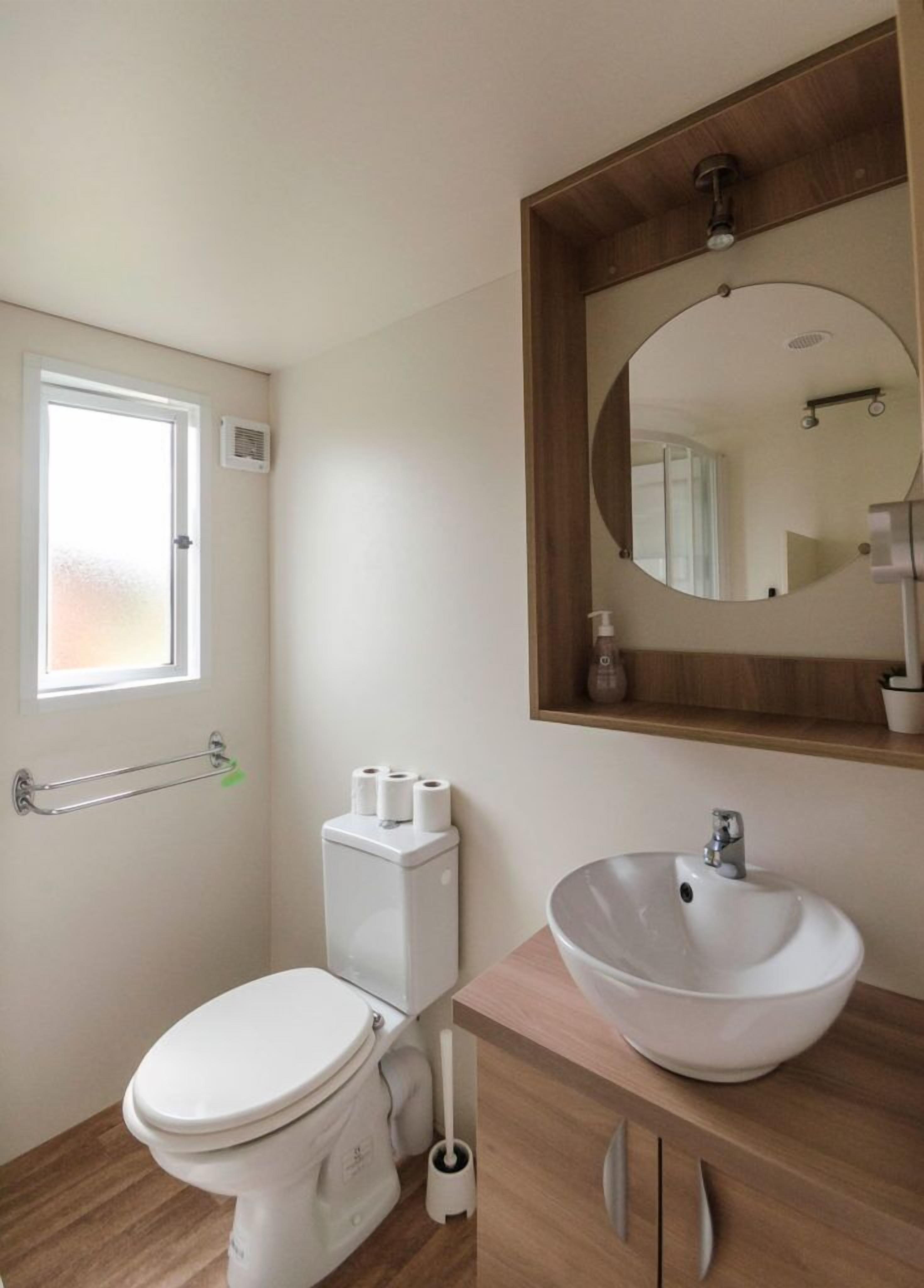 A small bathroom with a toilet, a sink, a mirror, and a window.