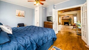 Une chambre dotée d’un grand lit, d’un ventilateur de plafond, d’une télévision et d’une cheminée située dans le salon attenant.