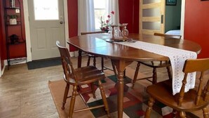 Une salle à manger avec une table en bois, quatre chaises, un chemin de table en dentelle et un vase rempli de fleurs.