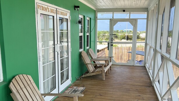 A covered porch with wooden chairs and a table, green walls, and a view of the beach. - Cozy, comfortable, secure home with pool, outside San Pedro near Secret Beach (San Pedro)