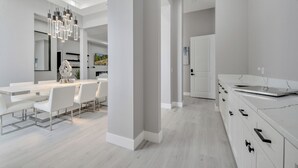 A modern kitchen with white cabinetry, a long countertop, and a dining area with white chairs. - Amazing Mansion on Toho (Kissimmee)