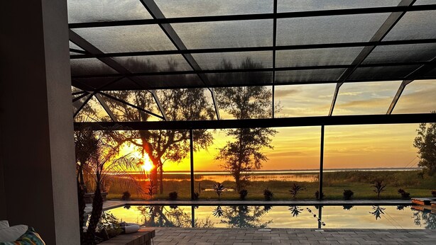 A terrace with a patterned floor, a seating area with cushions, and a view of a sunset over a body of water. - Amazing Mansion on Toho (Kissimmee)