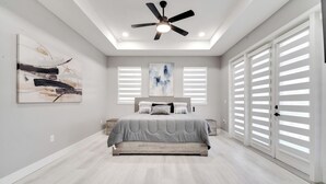 A bedroom with a bed, ceiling fan, artwork, and large windows. - Amazing Mansion on Toho (Kissimmee)