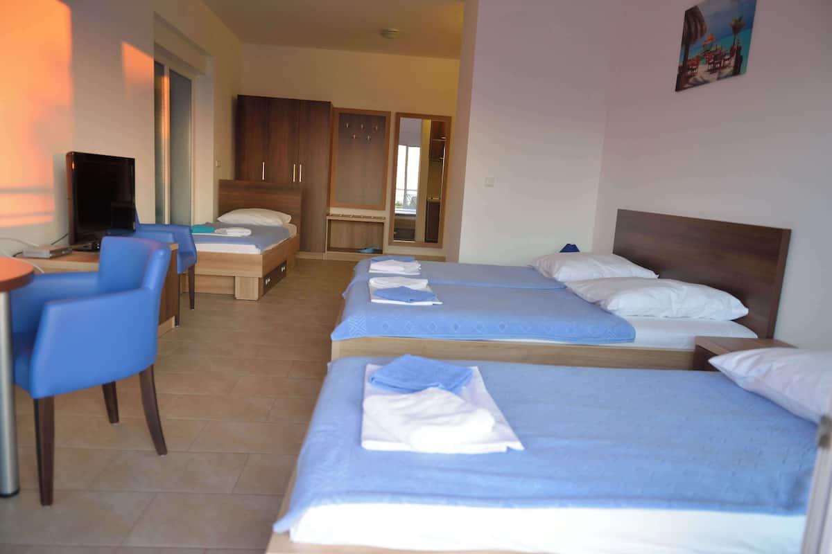 A hotel room with three beds, a desk with a chair, a TV, and a wardrobe.