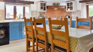A kitchen with blue cabinets, wooden chairs, and a table with a patterned tablecloth. - 3 bedroom accommodation in Hartland (Hartland)