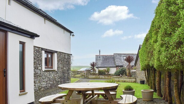 A patio area with a wooden table and benches, surrounded by a stone wall and a well-maintained lawn. - 3 bedroom accommodation in Hartland (Hartland)