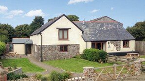 A two-story house with a stone facade, a sloped roof, and a fenced yard with a picnic table. - 3 bedroom accommodation in Hartland (Hartland)
