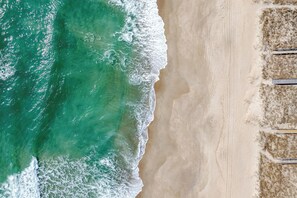 An aerial view of a beach with waves, sand, and a few umbrellas.
