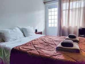 Une chambre d’hôtel avec un lit, une table de chevet, une fenêtre avec des rideaux et une porte.