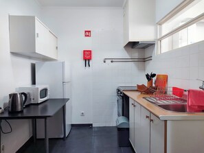 A compact kitchen with white cabinets, a microwave, a kettle, and a sink with a dish rack. - Bernardo's Place (Ponta Delgada)