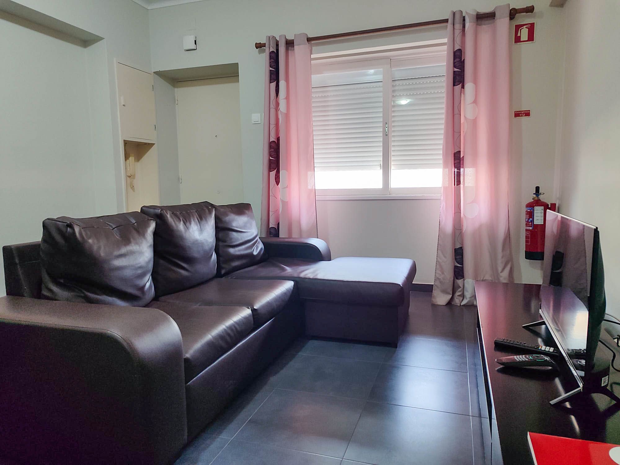 Una sala de estar con un sofá de cuero oscuro, un televisor de pantalla plana y un extintor de incendios fijado a la pared.
