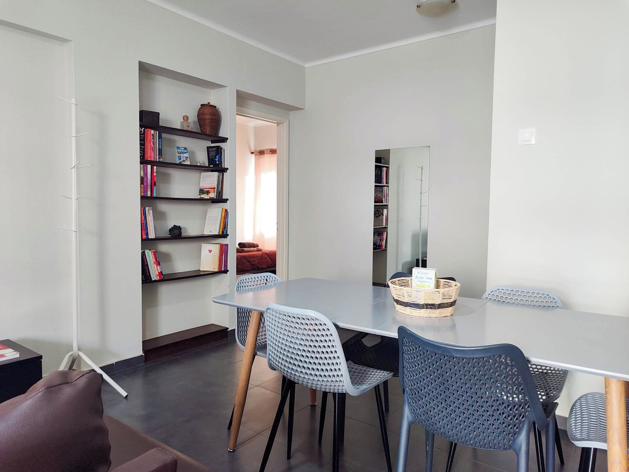 A modern dining area with a large table and chairs, surrounded by bookshelves and a small seating area.