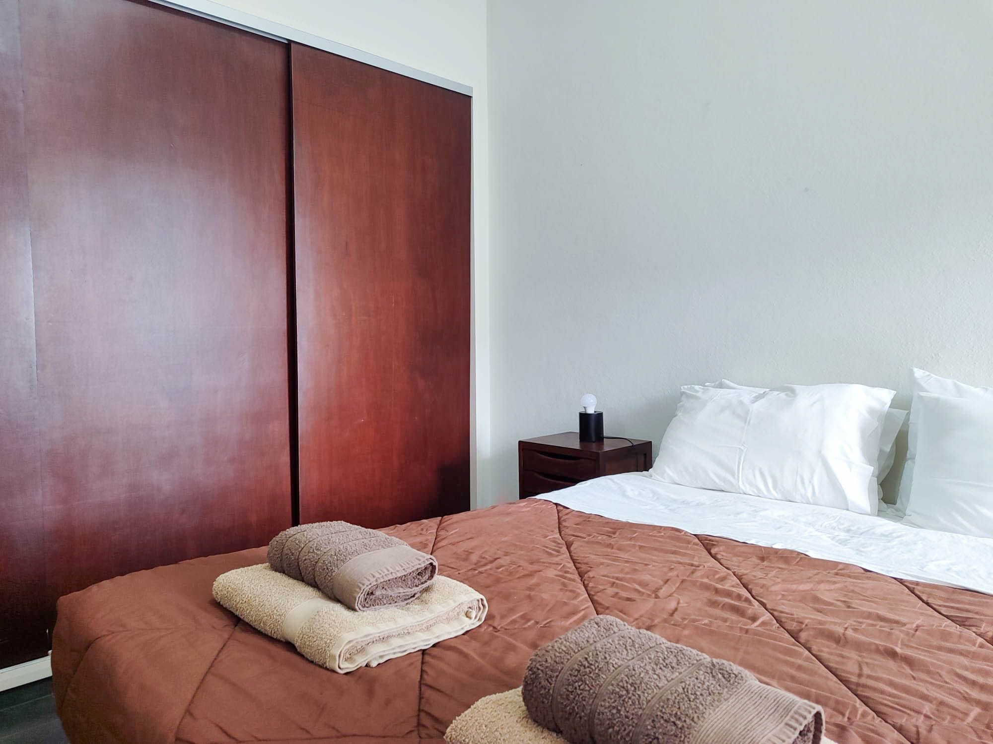 Une chambre d’hôtel avec un grand lit, une armoire, une table de chevet et une lampe.