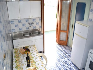 Cocina compacta con lavabo, refrigerador y mesa con mantel estampado de frutas.