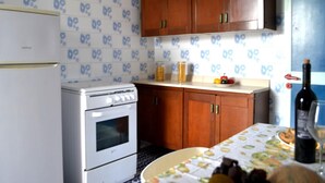 A kitchen with a refrigerator, stove, wooden cabinets, and a table with a fruit bowl and wine bottle. - Charming Holiday Home in San Foca, Italy - Perfect for Families (Melendugno)
