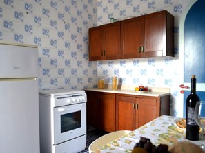 Una cocina con refrigerador, estufa, armarios de madera y una mesa con frutero y botella de vino.