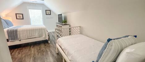 A bedroom with two beds, a ceiling fan, a window with blinds, a dresser, and a television.