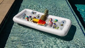 Une piscine avec un flotteur servant de glacière, contenant des boissons, une tranche de pastèque et un ananas.