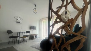A living room with a sofa, chairs, a coffee table, a TV, and a decorative tree structure. - Gite Les Mirettes Entre Terre et mer Avec Piscine, Salle de Jeux (Pornic)