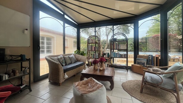 A spacious room with a large window, a wicker sofa, a coffee table, and a bookshelf. - Gite Les Mirettes Entre Terre et mer Avec Piscine, Salle de Jeux (Pornic)