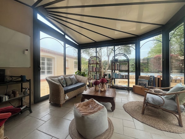 A spacious room with a large window, a wicker sofa, a coffee table, and a bookshelf.