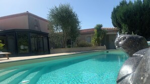 A swimming pool with clear water, surrounded by a tiled deck and a building with a tiled roof. - Gite Les Mirettes Entre Terre et mer Avec Piscine, Salle de Jeux (Pornic)