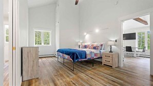 Un dormitorio con cama, mesita de noche, lámpara y vistas al exterior.