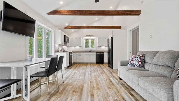 Una cocina moderna con armarios blancos, una zona de comedor con mesa y sillas, y un sofá gris con cojines estampados.