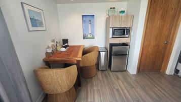 A compact kitchen with a wooden table, two chairs, a refrigerator, a microwave, and a cabinet.