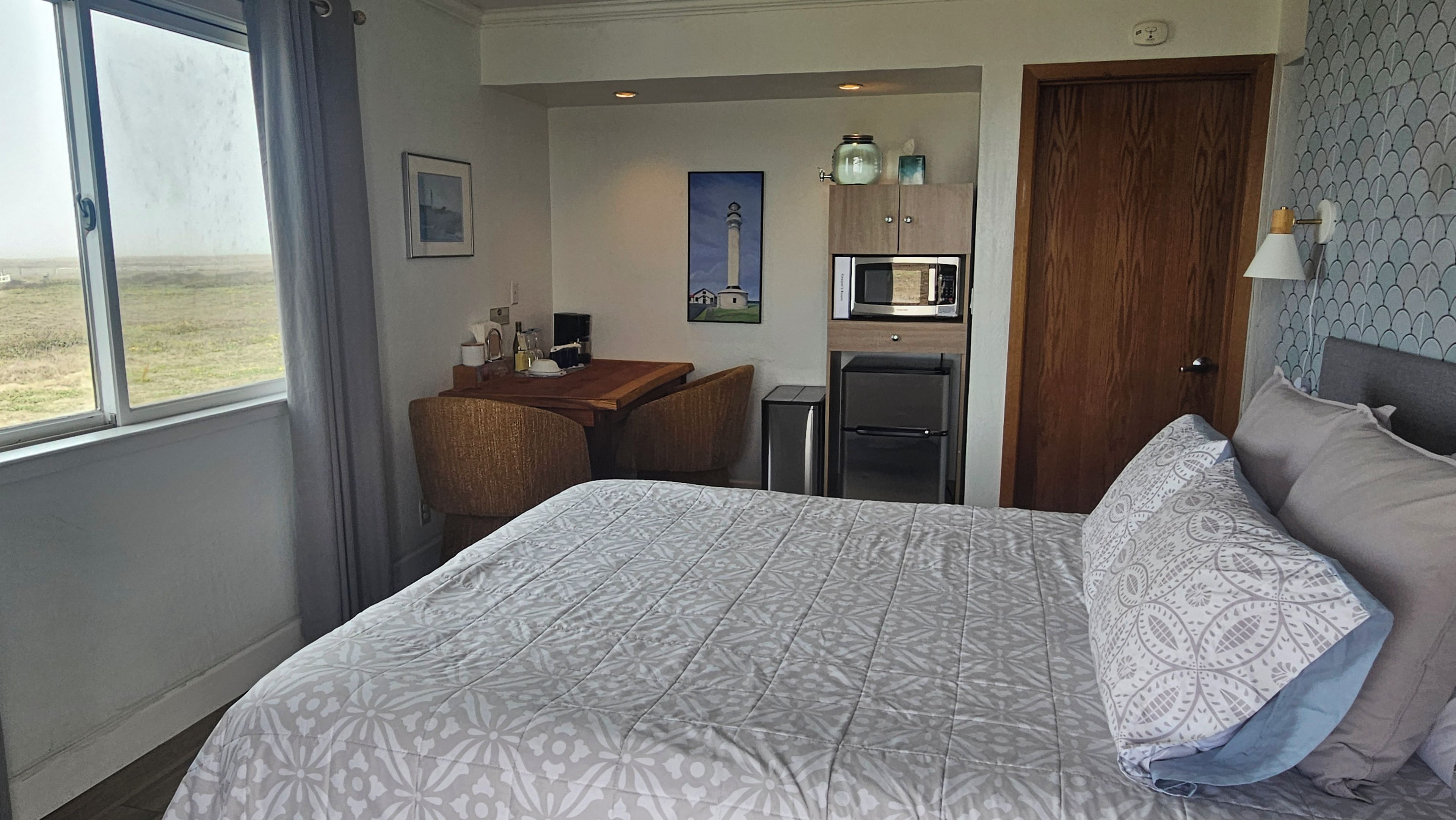 A hotel room with a bed, a desk, a refrigerator, and a microwave.