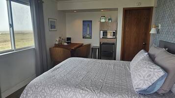 A hotel room with a bed, a desk, a refrigerator, and a microwave.