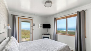 A bedroom with a bed, a television, a small table with a heater, and a view of the sea through a window. - Point Arena Lighthouse - Keeper's Room (Point Arena)