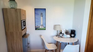 A small room with a wooden cabinet, a refrigerator, a table with two chairs, a coffee maker, and a painting of a lighthouse. - Point Arena Lighthouse - Keeper's Room (Point Arena)
