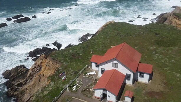 A coastal house with a red roof, situated on a grassy cliff overlooking the ocean. - Point Arena Lighthouse - Keeper's Room (Point Arena)