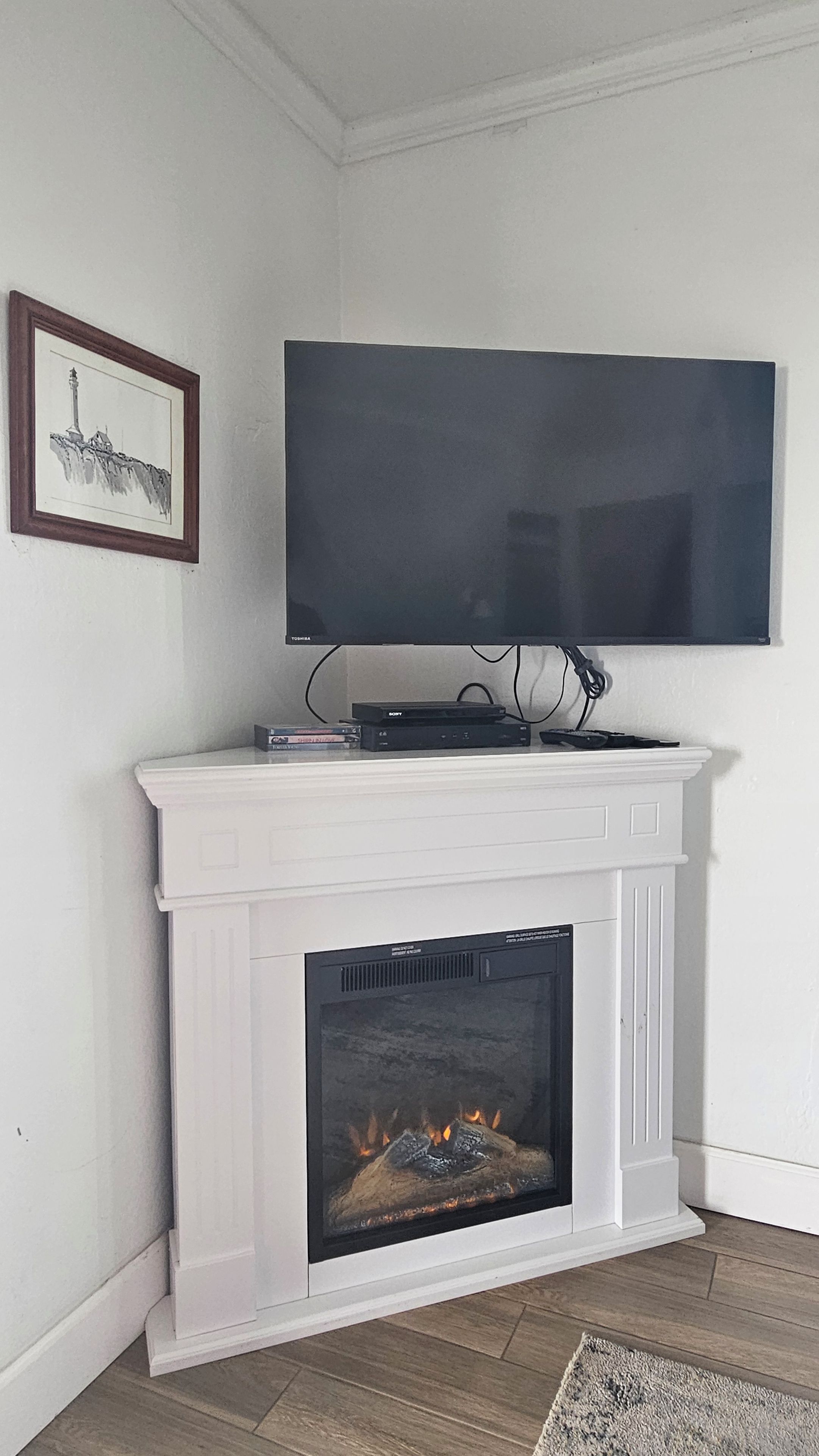 Ein weißer Kamin mit darüber montiertem Fernseher und einem gerahmten Bild an der Wand.
