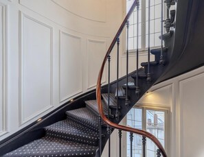 A staircase with a black handrail and patterned carpet, leading to a landing with a window.