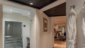 A hotel corridor with a glass-enclosed shower area, a treadmill in the background, and a white robe hanging on the wall. - Hotiday Room Collection - Paris Arc de Triomphe (Paris)
