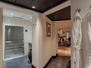 A hotel hallway with a glass door leading to a bathroom, a treadmill, and a rack of white robes. - Hotiday Room Collection - Paris Arc de Triomphe (Paris)