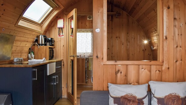 Un intérieur de chalet chaleureux avec une kitchenette, un canapé agrémenté de coussins à motifs animaliers et une lucarne.