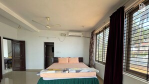 Ein Schlafzimmer mit einem Bett, einer Klimaanlage, einem Deckenventilator, einem Fenster mit Vorhängen und einer Tür zu einem anderen Raum.