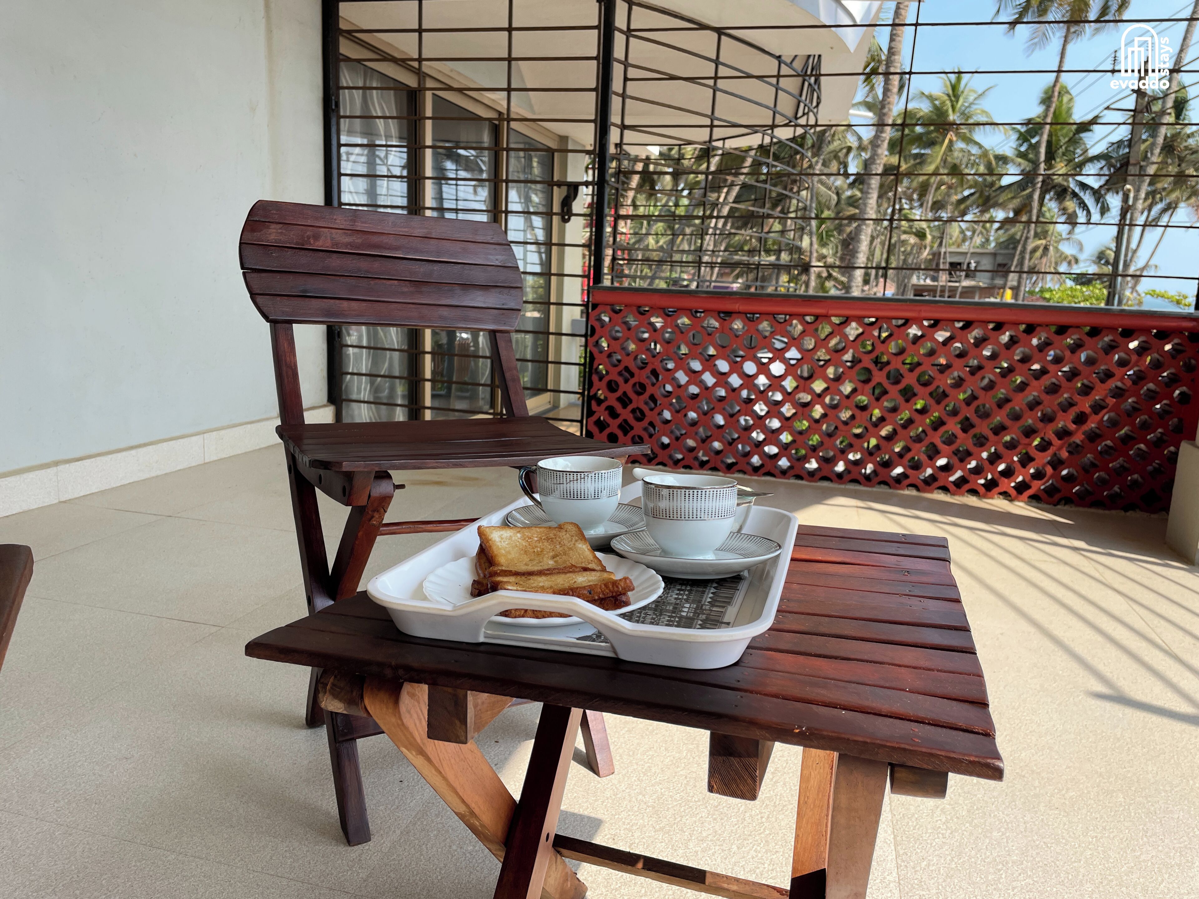 A wooden table with a tray containing a cup, a teapot, and a plate with toast and a sandwich.