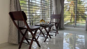 Una habitación con vistas a palmeras a través de celosías, una mesa de madera con un plátano y una taza, y dos sillas de madera.