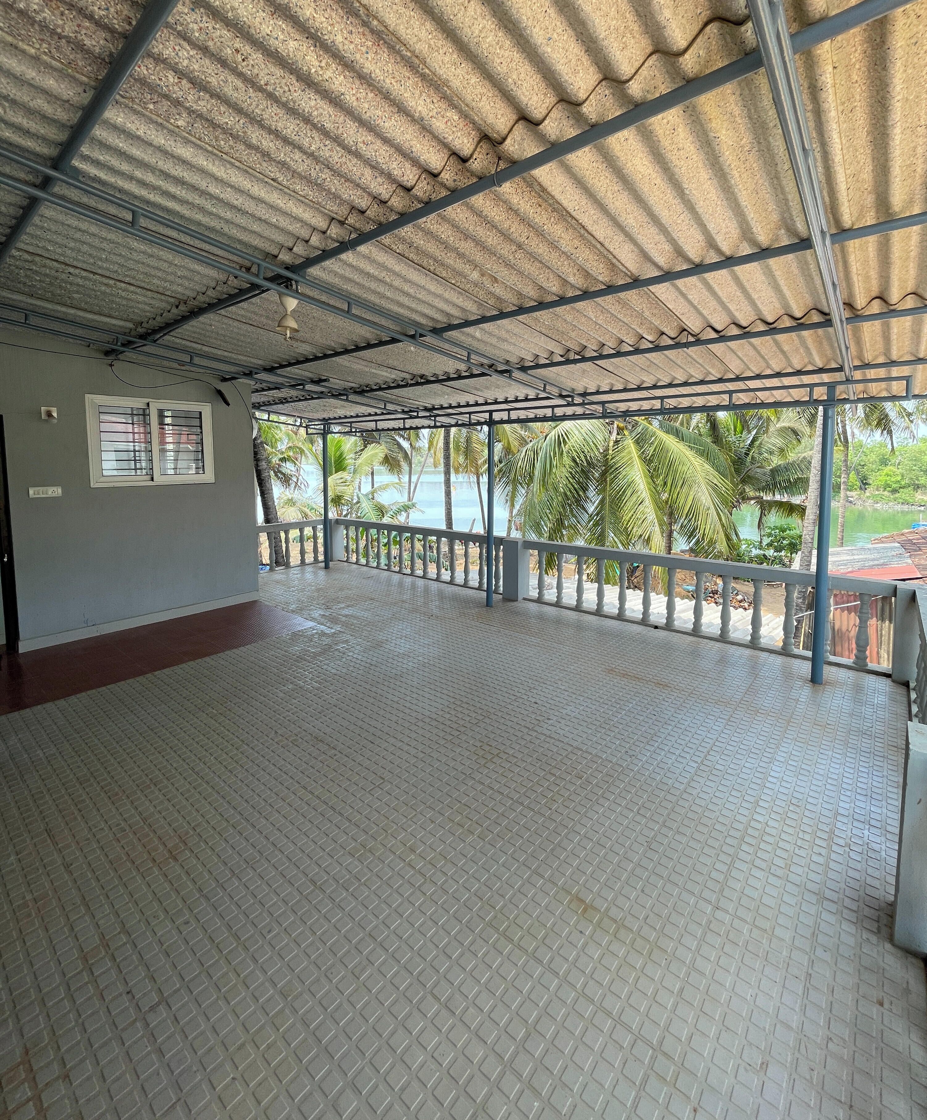 A spacious indoor area with a tiled floor, a metal roof, and a view of palm trees and water outside.