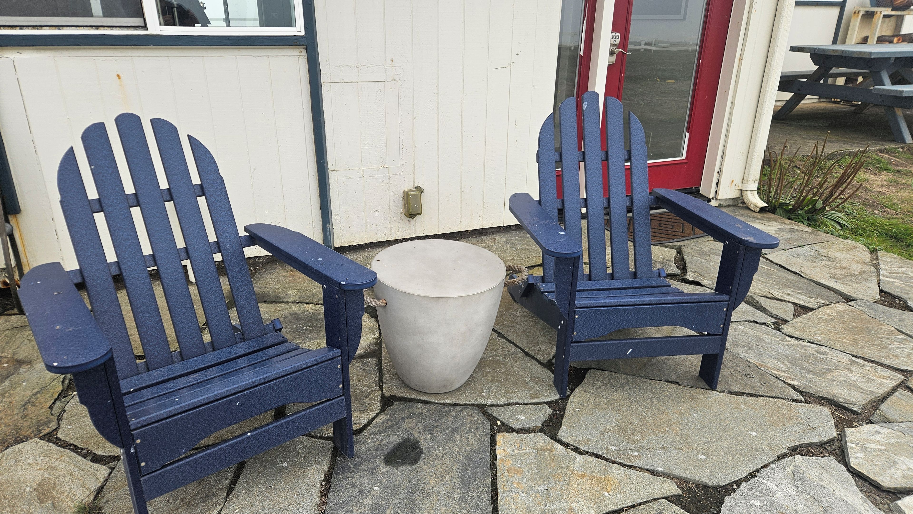 Zwei Adirondack-Stühle mit einem runden Tisch davor, auf einer Steinterrasse platziert.